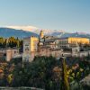 Ciudad, fortaleza y palacio de la Alhambra en el pueblo de Granada rodeada de vegetación y de fondo las sierras nevadas.