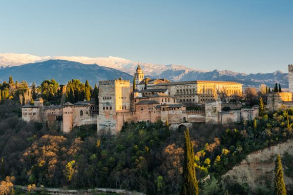 Ciudad, fortaleza y palacio de la Alhambra en el pueblo de Granada rodeada de vegetación y de fondo las sierras nevadas.