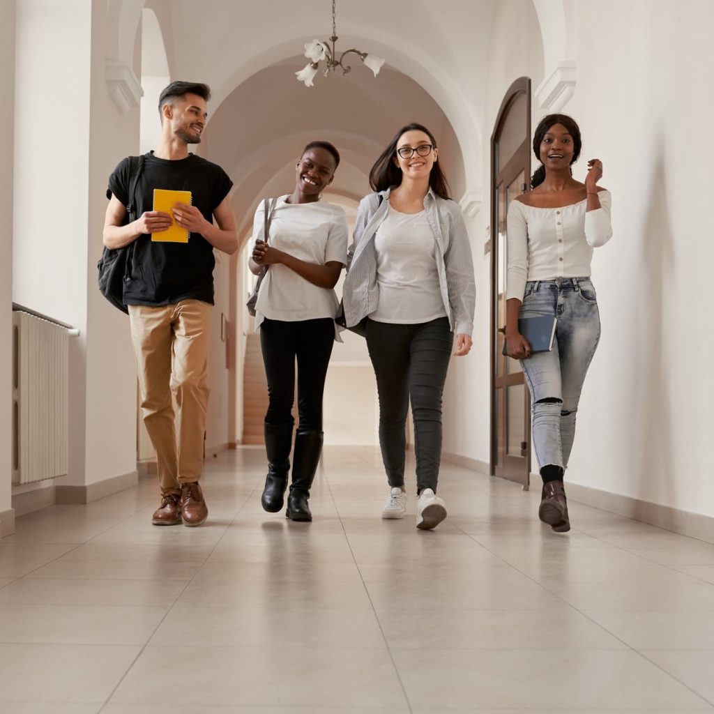 Grupo de jóvenes sonrientes caminando caminando por pasillo de edificio.