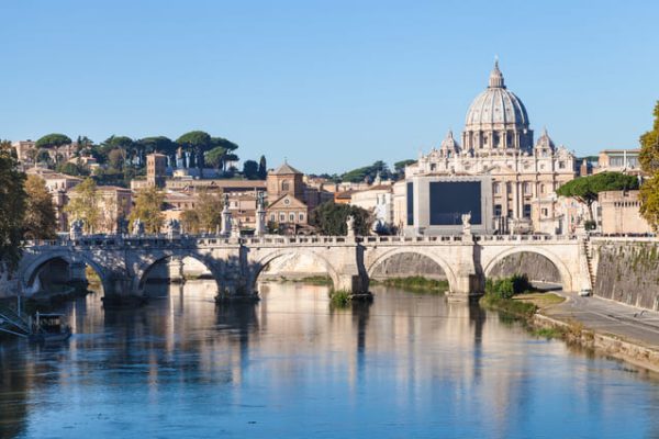Imagen de la ciudad del Vaticano a lo lejos. Puente y rio en día soleado.