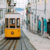 Tranvía amarillo y blanco en las calles de Lisboa Portugal con el mar de fondo.