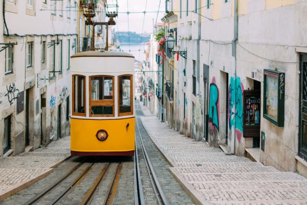 Tranvía amarillo y blanco en las calles de Lisboa Portugal con el mar de fondo.