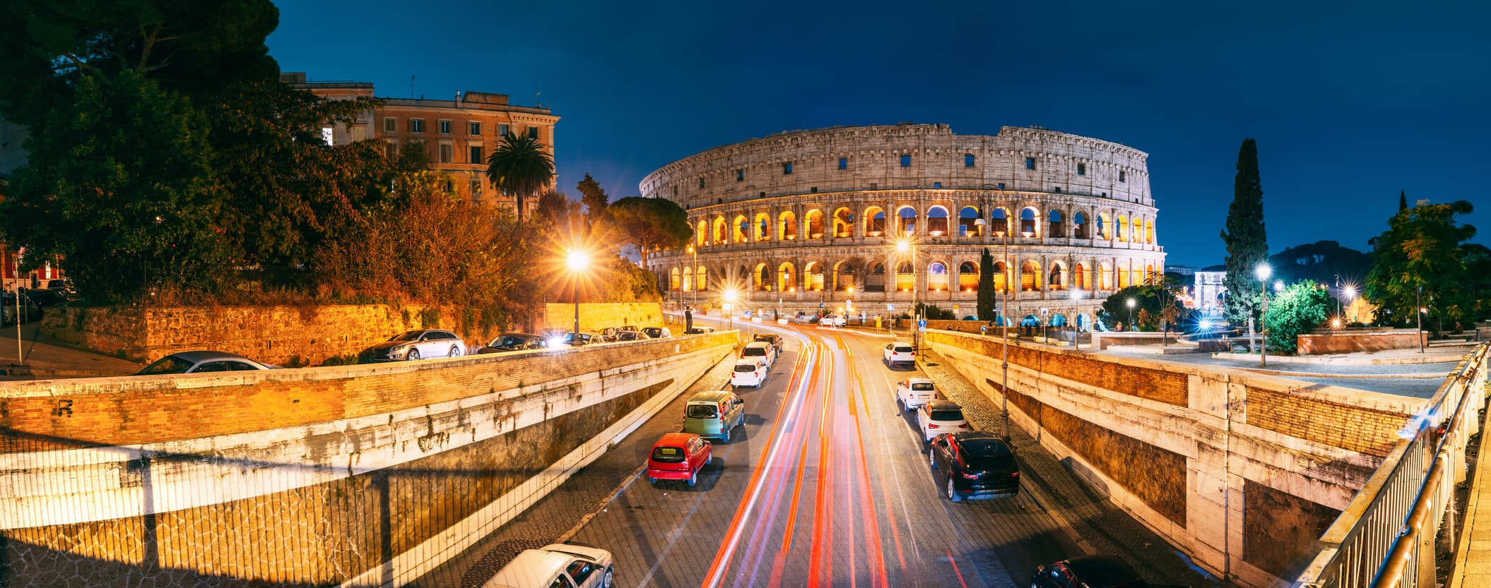 Fotografía de las calles iluminadas y el Coliseo en Roma Italia al atardecer. Entorno, luces, coches, atardecer.